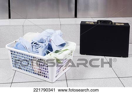 Stock Image - Laundry basket near a briefcase in a laundromat. Fotosearch