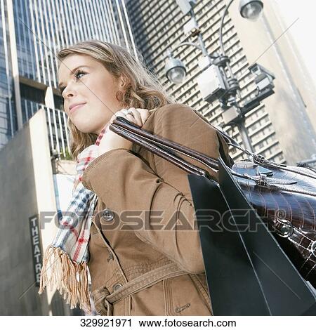 Stock Image - Low angle view of a teenage girl carrying a shopping bag and a purse. Fotosearch
