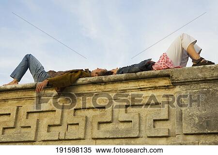 Low angle view of a young couple lying on a stone wall View Large Photo Image Stock Photography - Low angle view of a young couple lying on a stone wall. Fotosearch