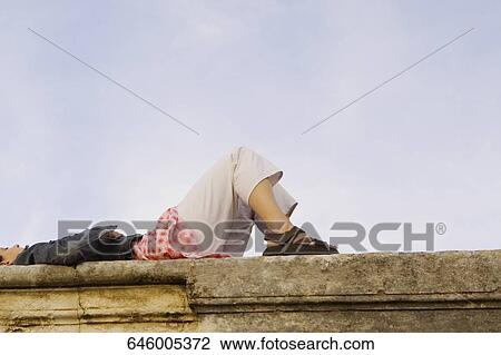 Low angle view of a young woman lying on a stone wall View Large Photo Image Stock Image - Low angle view of a young woman lying on a stone wall. Fotosearch