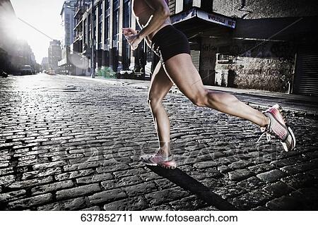Stock Image - Low section view of a woman jogging in the street. Fotosearch