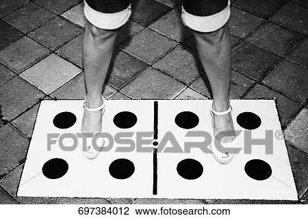 Stock Image - Low section view of a woman standing with her legs apart on dice drawn on the floor. Fotosearch