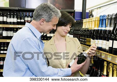 Picture - Man and a woman buying wine bottle in a liquor store. Fotosearch