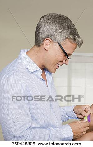 Stock Photography - Man applying bandage on his daughter's knee. Fotosearch