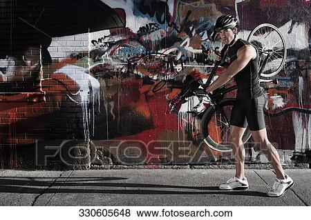 Man carrying a bicycle on his shoulders in front of a graffiti covered wall View Large Photo Image Stock Photo - Man carrying a bicycle on his shoulders in front of a graffiti covered wall. Fotosearch