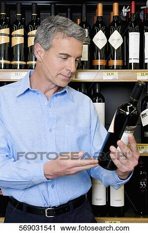 Stock Image - Man choosing wine in a supermarket. Fotosearch