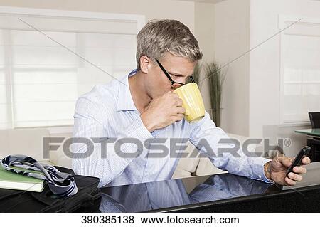 Man drinking coffee and text messaging on a mobile phone View Large Photo Image Stock Photo - Man drinking coffee and text messaging on a mobile phone. Fotosearch