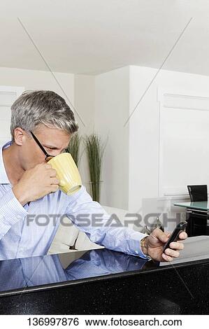 Stock Photograph - Man drinking coffee and text messaging on a mobile phone. Fotosearch