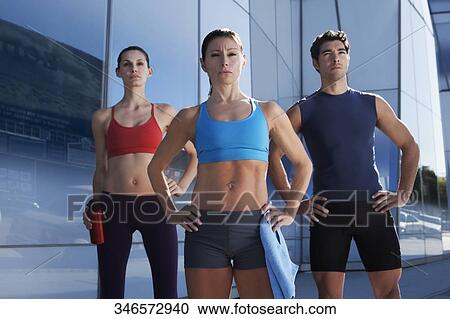 Stock Image - Man exercising with two women in front of a building. Fotosearch