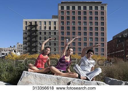 Stock Photo - Man exercising with two women on a rock. Fotosearch