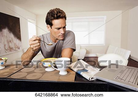 Picture - Man having breakfast and reading a newspaper. Fotosearch