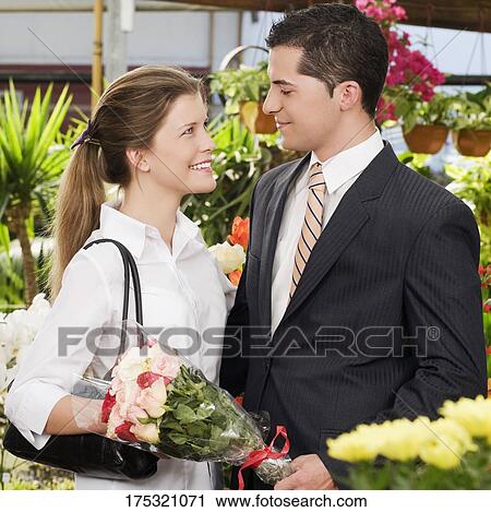 Man holding a bouquet of flowers with a woman smiling at him View Large Photo Image Stock Image - Man holding a bouquet of flowers with a woman smiling at him. Fotosearch