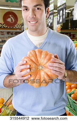 Man holding a pumpkin in a supermarket View Large Photo Image Stock Image - Man holding a pumpkin in a supermarket. Fotosearch