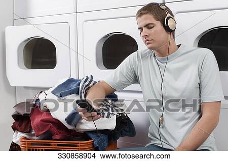 Picture - Man listening to an MP3 player in a laundromat. Fotosearch