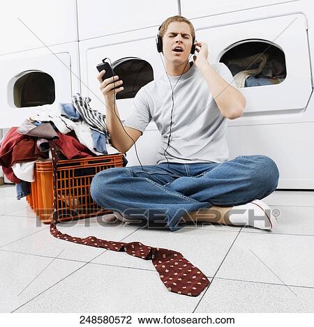 Stock Image - Man listening to an MP3 player in a laundromat. Fotosearch