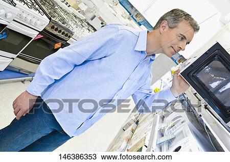 Man looking at a microwave oven in a supermarket View Large Photo Image Stock Image - Man looking at a microwave oven in a supermarket. Fotosearch