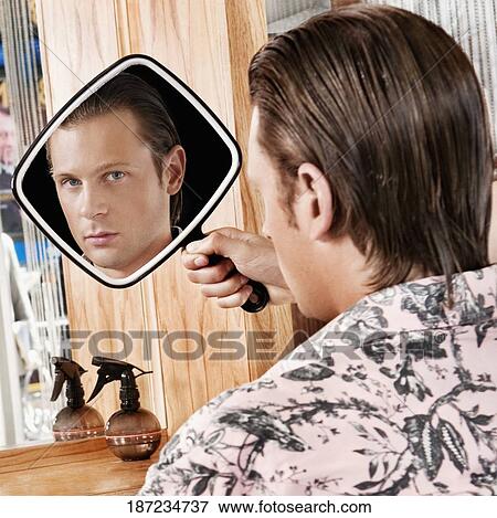 Stock Photo - Man looking himself in a mirror after a haircut. Fotosearch