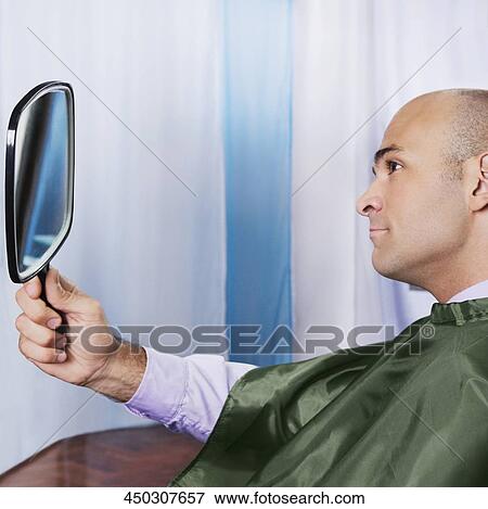 Stock Photo - Man looking himself in a mirror after a haircut. Fotosearch