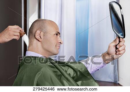 Man looking himself in a mirror after a haircut View Large Photo Image Stock Photograph - Man looking himself in a mirror after a haircut. Fotosearch