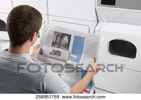 Man reading a newspaper in a laundromat View Large Photo Image Stock Photo - Man reading a newspaper in a laundromat. Fotosearch