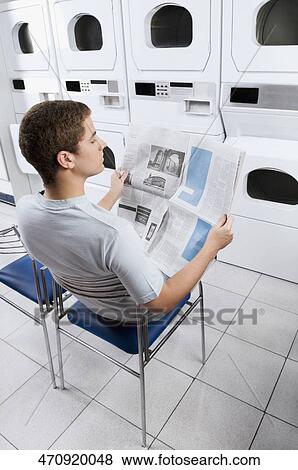 Stock Photo - Man reading a newspaper in a laundromat. Fotosearch