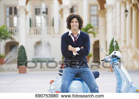 Stock Image - Man sitting on a moped with his arm crossed, Biltmore Hotel, Coral Gables, Florida, USA. Fotosearch