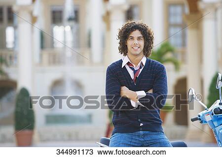 Stock Image - Man sitting on a moped with his arms crossed, Biltmore Hotel, Coral Gables, Florida, USA. Fotosearch