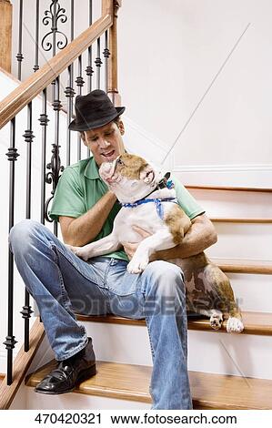 Stock Image - Man sitting on a staircase and carrying his dog. Fotosearch