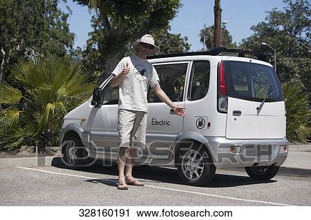 Stock Image - Man standing near an electric car, Los Angeles, California, USA. Fotosearch