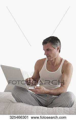 Man working on a laptop on the bed View Large Photo Image Stock Image - Man working on a laptop on the bed. Fotosearch
