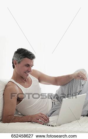 Stock Photo - Man working on a laptop on the bed. Fotosearch