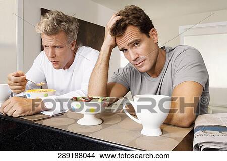 Picture - Men frowning at bowls of cereal and fruits. Fotosearch