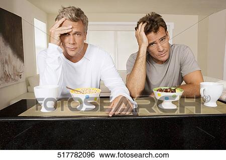 Stock Photograph - Men frowning at bowls of cereal and fruits. Fotosearch