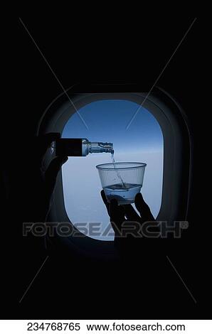Stock Photography - Person pouring whiskey into a glass in front of an airplane window. Fotosearch