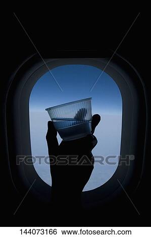 Person's hand holding a glass of water in front of an airplane window View Large Photo Image Stock Photograph - Person's hand holding a glass of water in front of an airplane window. Fotosearch