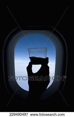 Stock Photo - Person's hand holding a glass of wine in front of an airplane window. Fotosearch