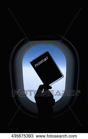 Stock Image - Person's hand holding a passport in front of an airplane window. Fotosearch