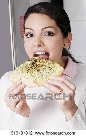 Stock Image - Portrait of a female chef eating a slice of pizza. Fotosearch
