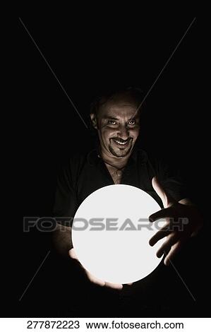 Stock Image - Portrait of a man holding a crystal ball and smiling. Fotosearch