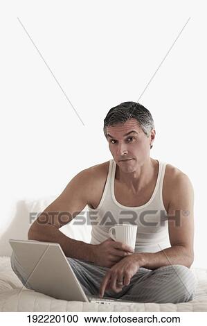 Portrait of a man working on a laptop on the bed View Large Photo Image Stock Image - Portrait of a man working on a laptop on the bed. Fotosearch