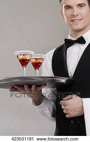 Stock Image - Portrait of a waiter holding a tray of martini glasses. Fotosearch