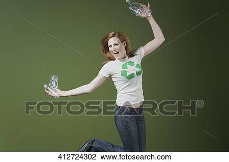 Stock Image - Portrait of a woman holding plastic bottles and jumping. Fotosearch