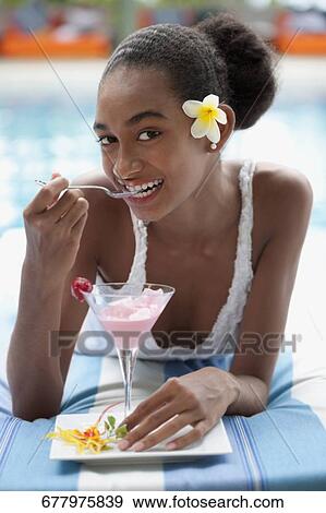 Stock Photo - Portrait of a woman lying at the poolside and eating ice cream. Fotosearch