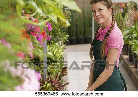 Stock Photograph - Portrait of a woman standing in a greenhouse and smiling. Fotosearch