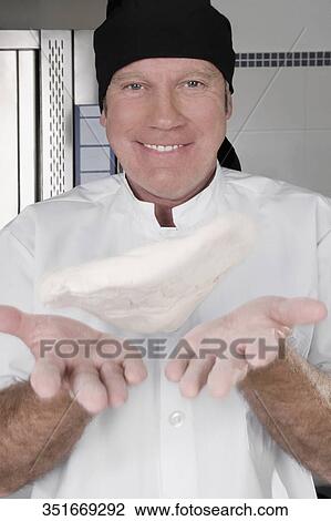 Stock Image - Portrait of chef throwing pizza dough. Fotosearch