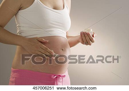 Stock Image - Pregnant woman applying moisturizer on her abdomen. Fotosearch