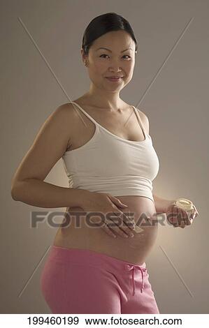 Pregnant woman applying moisturizer on her abdomen View Large Photo Image Stock Photo - Pregnant woman applying moisturizer on her abdomen. Fotosearch