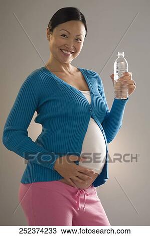 Stock Image - Pregnant woman holding a water bottle and smiling. Fotosearch