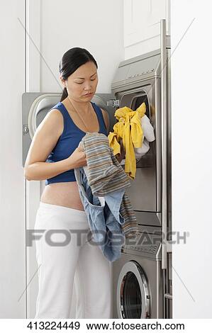 Pregnant woman holding clothes in front of a washing machine View Large Photo Image Stock Photo - Pregnant woman holding clothes in front of a washing machine. Fotosearch