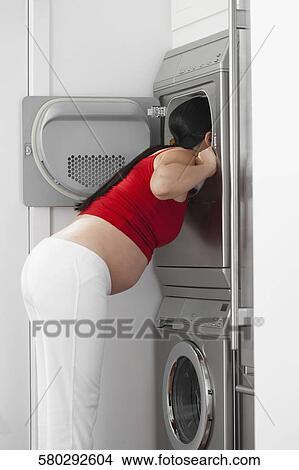 Pregnant woman looking into a washing machine View Large Photo Image Picture - Pregnant woman looking into a washing machine. Fotosearch